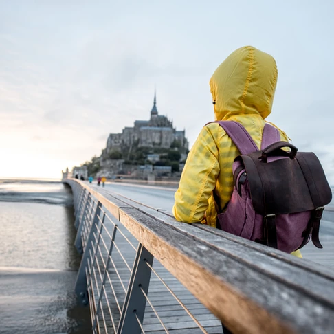 Photo of a person in a yellow jacket wearing a backpack, staring out across a body of water